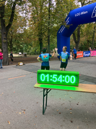 Im Vordergrund Uhr mit Laufzeitmessung auf 1:54:00, im Hintergrund Übergabe der Laufstaffel